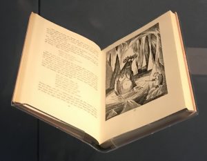 A book open at an illustrated page with a large troll-like version of Gollum towering over Bilbo.