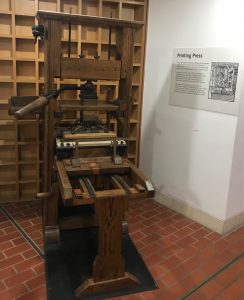 An old wooden printing press in an alcove in front of a wooden wall.