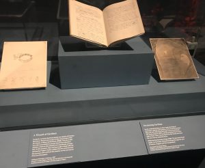 Hand-written books in a display case with explanatory notes.