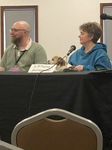 Two panelists at a table with a dog on the lap of one of them