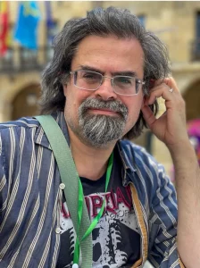 Author Adrian Tchaikovsky in relaxed outdoor post wearing striped shirt over black T