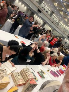 Long white covered tables with authors signing books and fans milling about