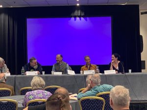 four panelists at a table sitting infront of a blue screen